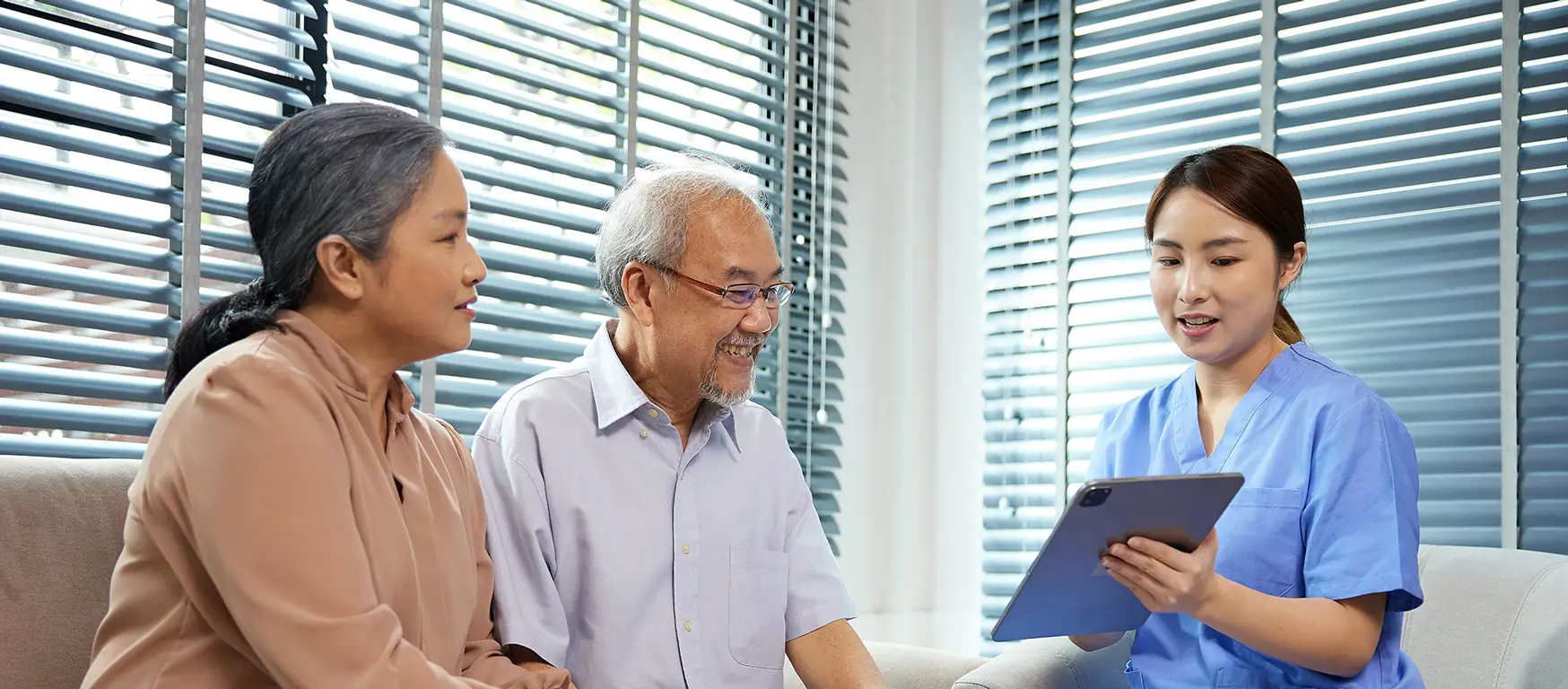 nurse sits on a couch with two elderly individuals, engaging in a friendly conversation.