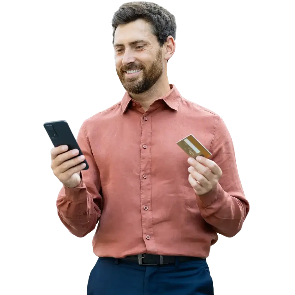 A man uses his smartphone and holds a credit card, likely making a purchase or managing finances.