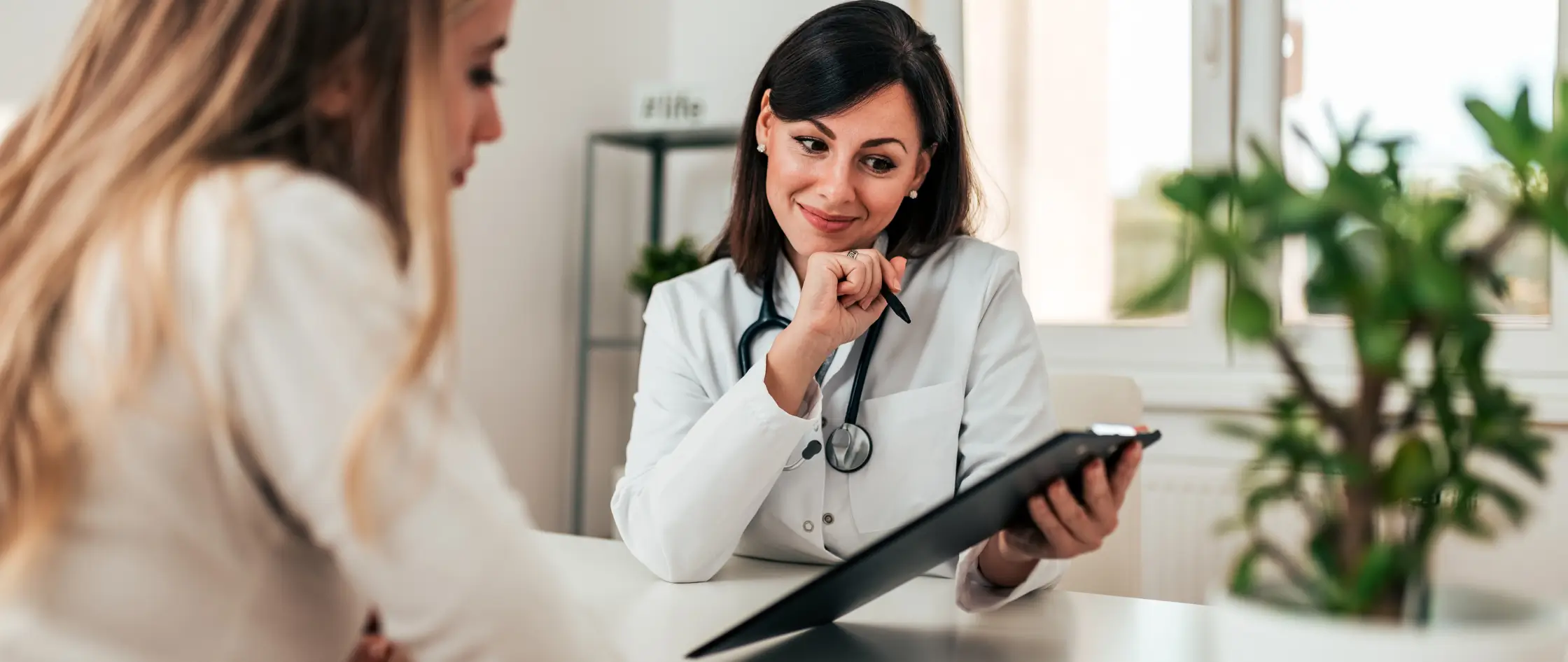 A woman discusses her health with a doctor while seated at a desk in a professional office setting.