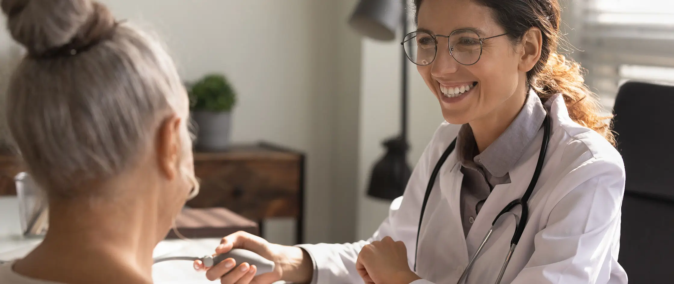 A woman discusses her health concerns while getting blood pressure checked with a doctor in a clinical setting.